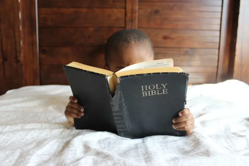 bible study showing a baby boy with a large bible covering his face and reading it